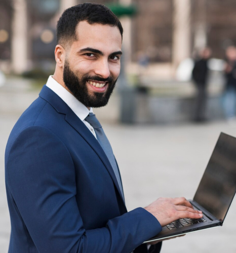 Homem de barba e terno azul com gravata sorrindo para a câmera enquanto segura um notebook, em ambiente externo desfocado, representando a contabilidade para advogados no Rio