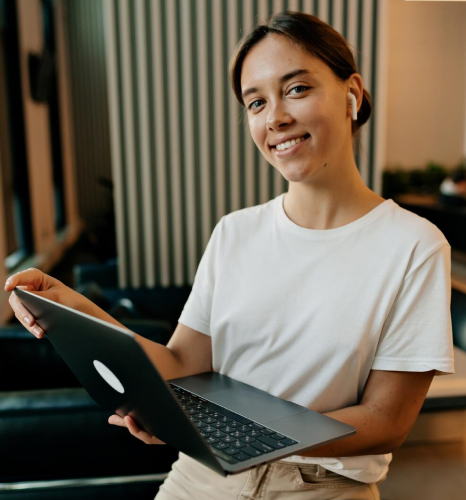 Mulher sorridente de camiseta branca e fone de ouvido sem fio segurando um tablet, em ambiente com painel de madeira ao fundo, representando a contabilidade para startups e infoprodutores