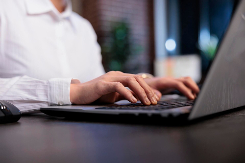 Mãos de uma pessoa de camisa branca digitando em um notebook sobre uma mesa escura, em uma rotina de contabilidade para advogados no Rio
